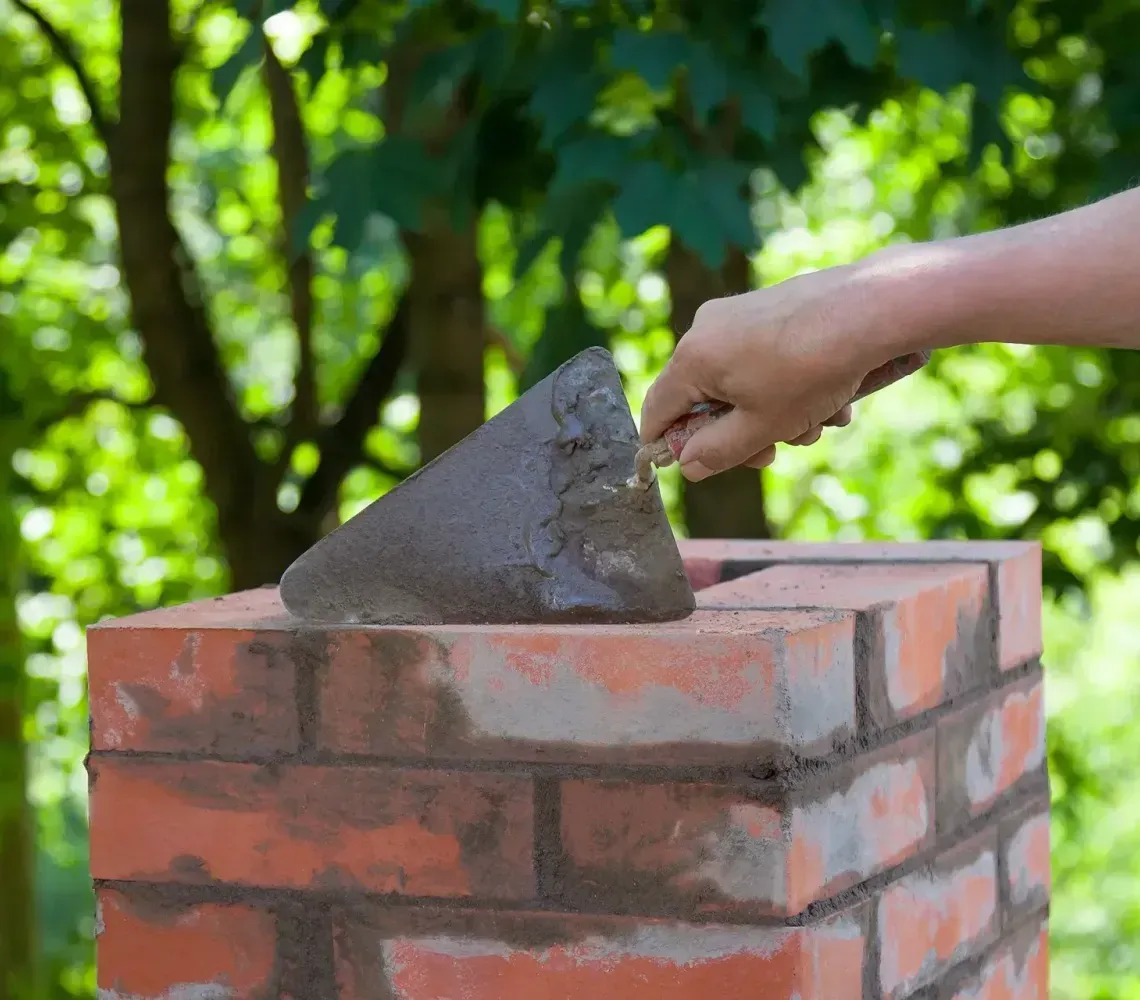 Hand placing mortar with a trowel on a brick wall outdoors