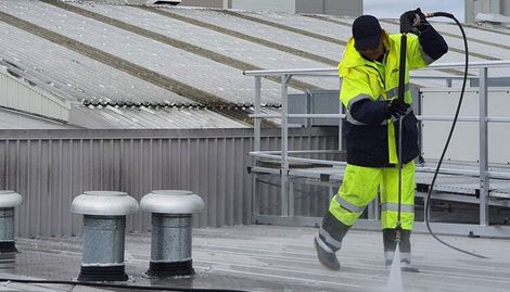 A man in a yellow jacket is coating a roof with a hose