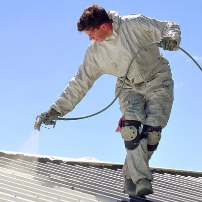 A man in a white suit is spraying paint on a roof