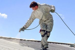 A man is spraying paint on the roof of a building.