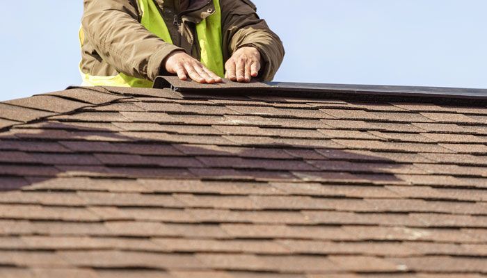 A man in a yellow vest is working on a roof