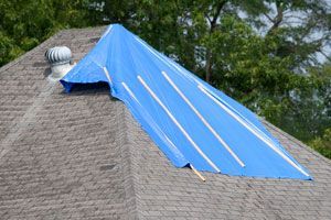 A blue tarp is covering the roof leak on a house.