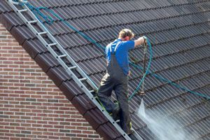 A man is cleaning the roof of a building with a high pressure washer.