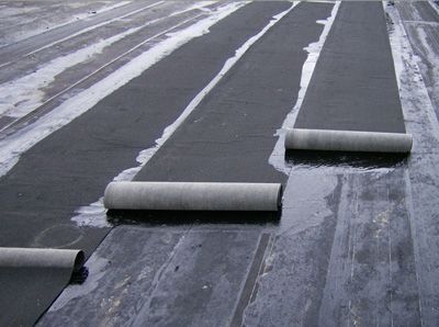 Two rolls of modified bitumen being rolled onto a roof.