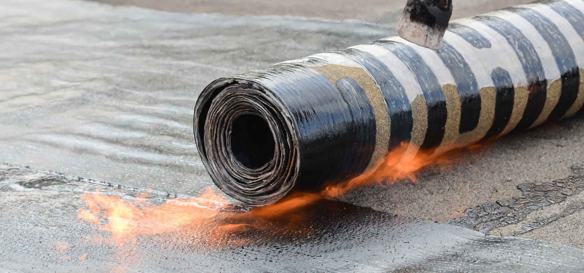 A person is laying a roll of asphalt on the ground.