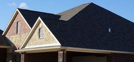 A brick house with a black roof and a blue sky in the background