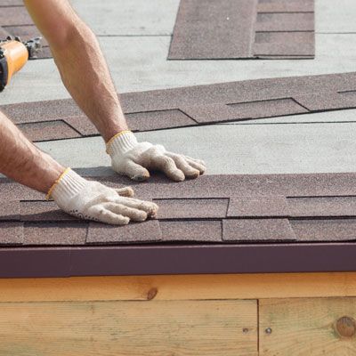 A man is installing shingles on a roof with a drill.