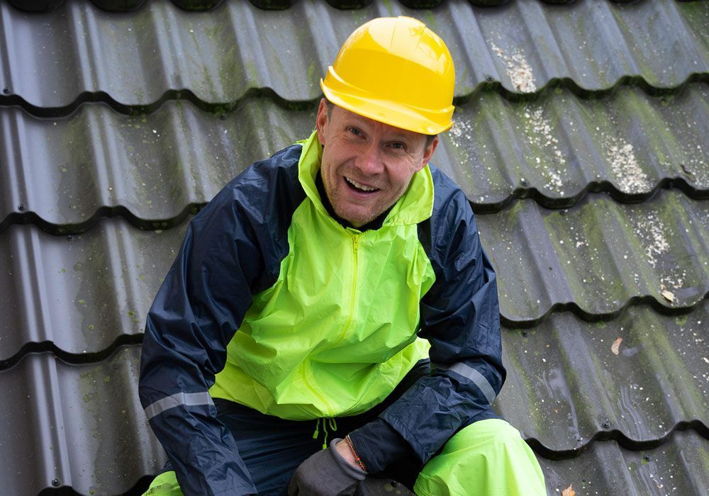 A man wearing a yellow hard hat is sitting on a roof.