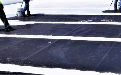 Two men are painting a black roof with white silicone coatings