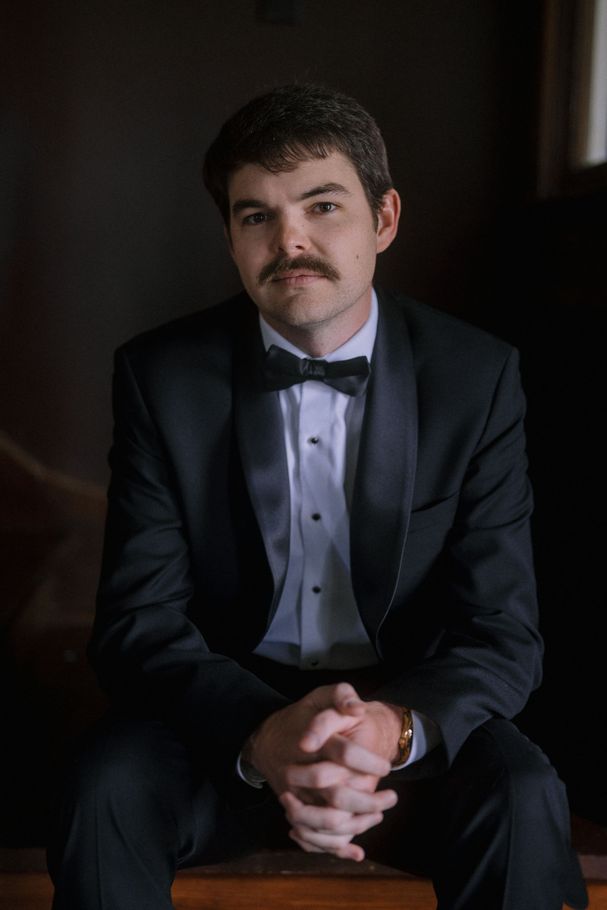 a picture of Hunter Garrett Hall in a tuxedo with a bow tie, seated, hands clasped, looking at the camera.