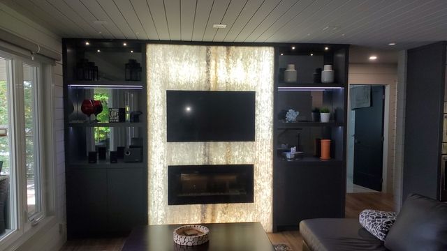 Living room with a backlit stone feature wall, TV, fireplace, and dark cabinets on either side.