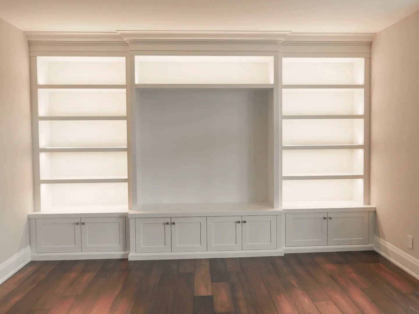 An empty room with white cabinets and shelves and a wooden floor.