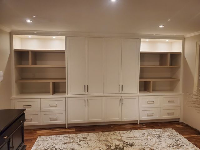 A living room with white cabinets , shelves , drawers and a rug.