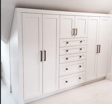 A large white cabinet with drawers under a slanted ceiling