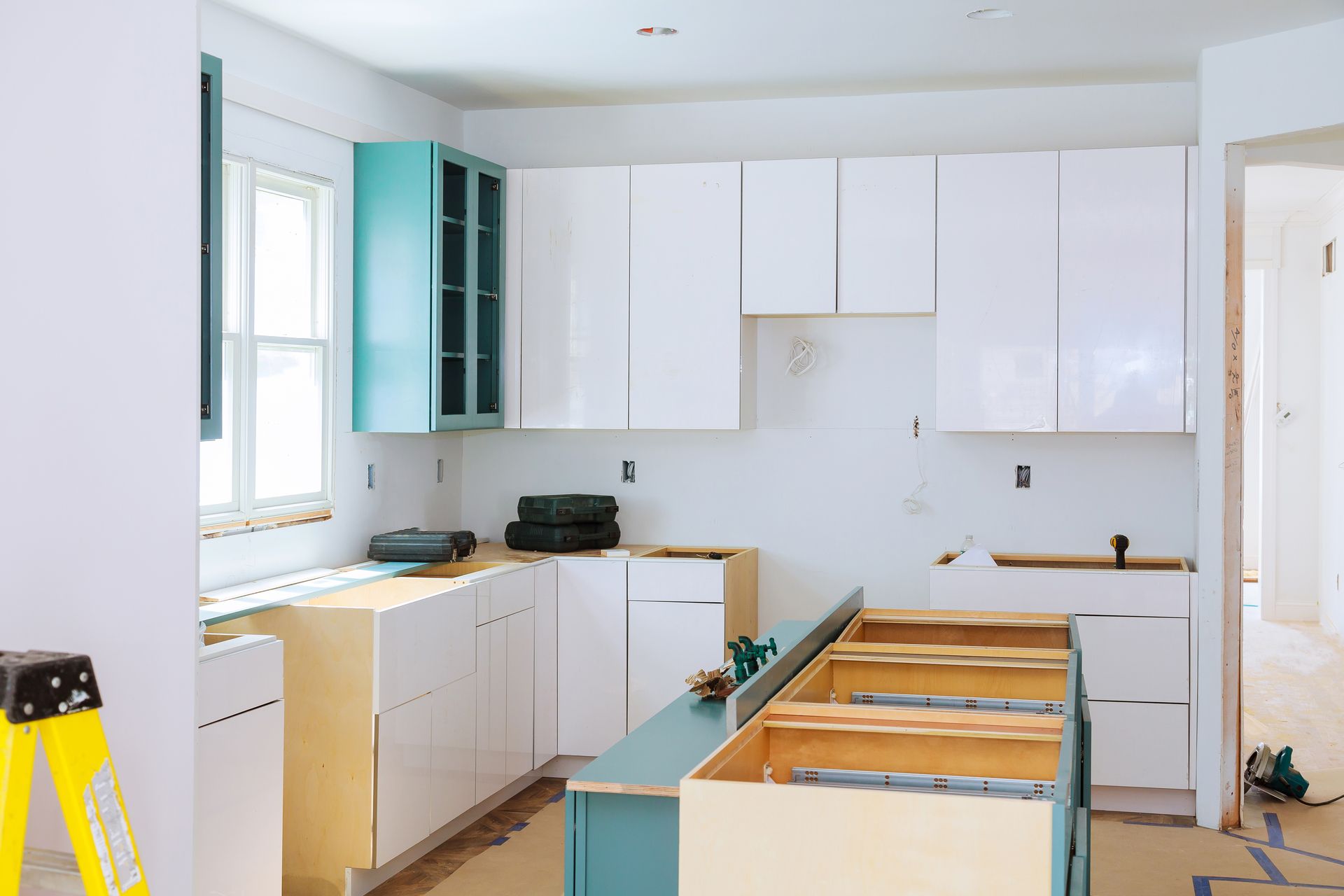 Kitchen under construction with white cabinets, teal accents, and unfinished cabinetry.