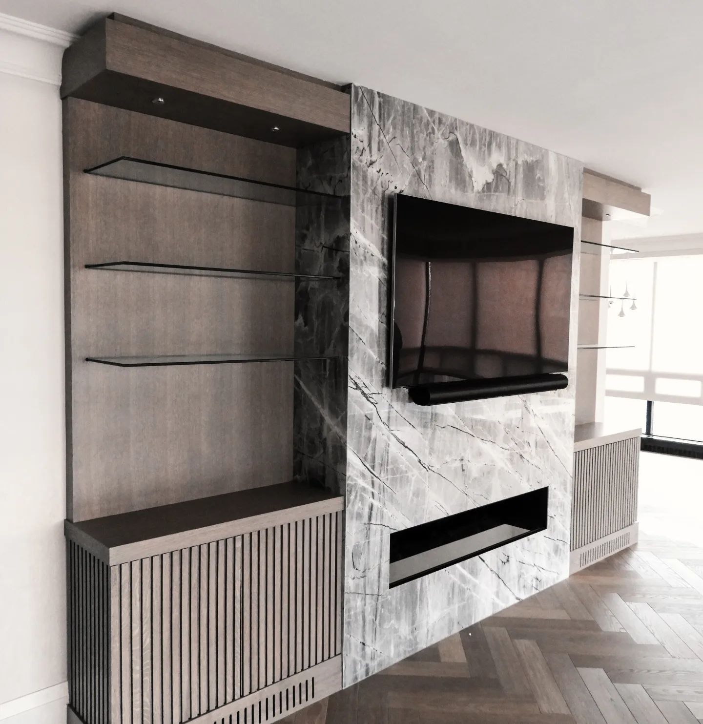 Wooden media center with marble accent wall, TV, shelves, and fireplace.