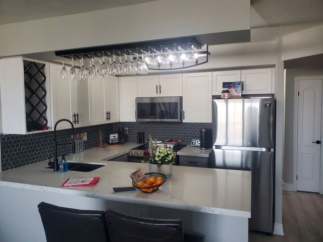 Modern kitchen with white cabinets, stainless steel appliances, and a bar area.