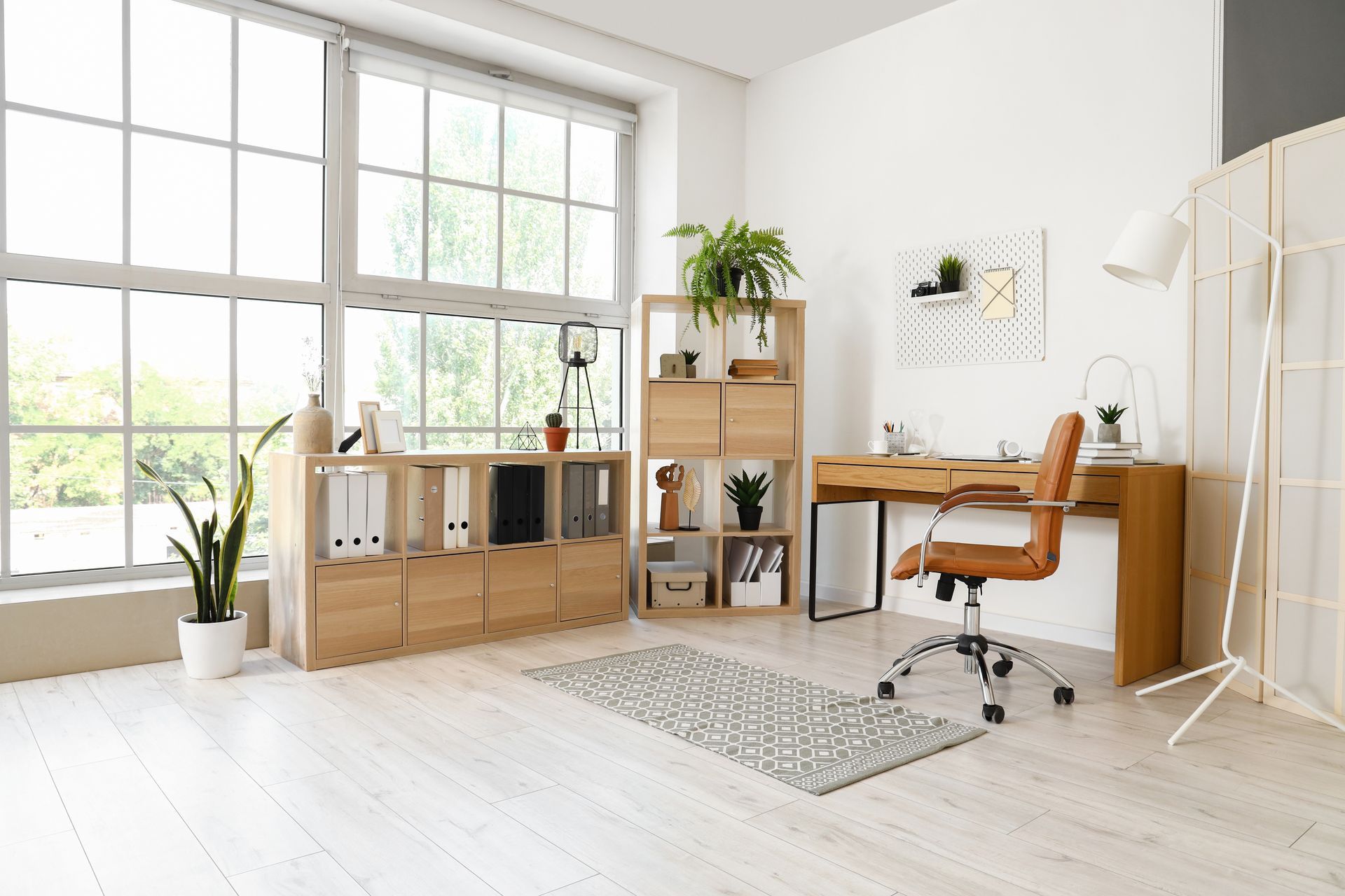 Bright home office with desk, shelving, plants, large window, wood floor.