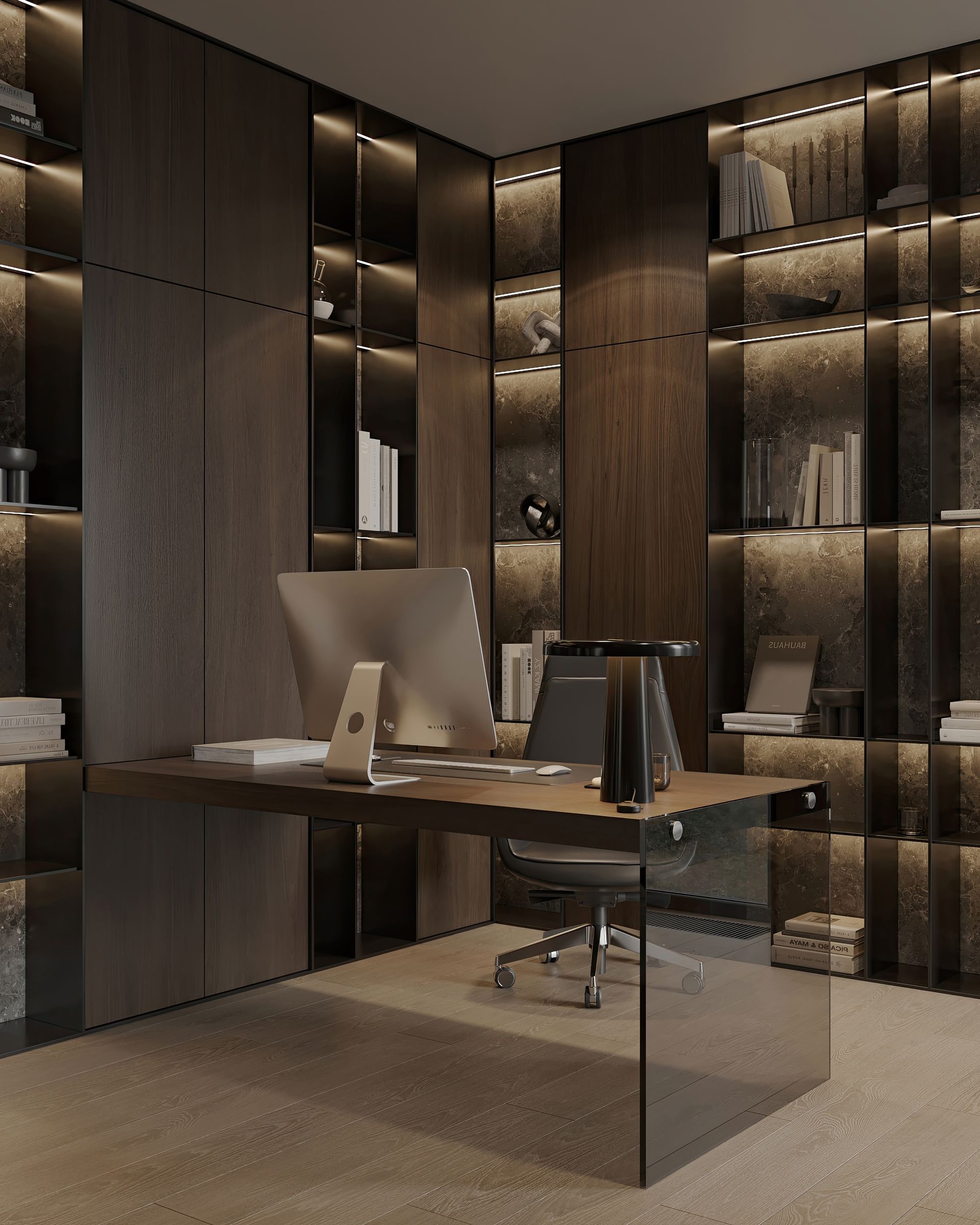 A modern home office with dark wood paneling and built-in shelves lit with warm lights. There is a desk with a computer and chair.