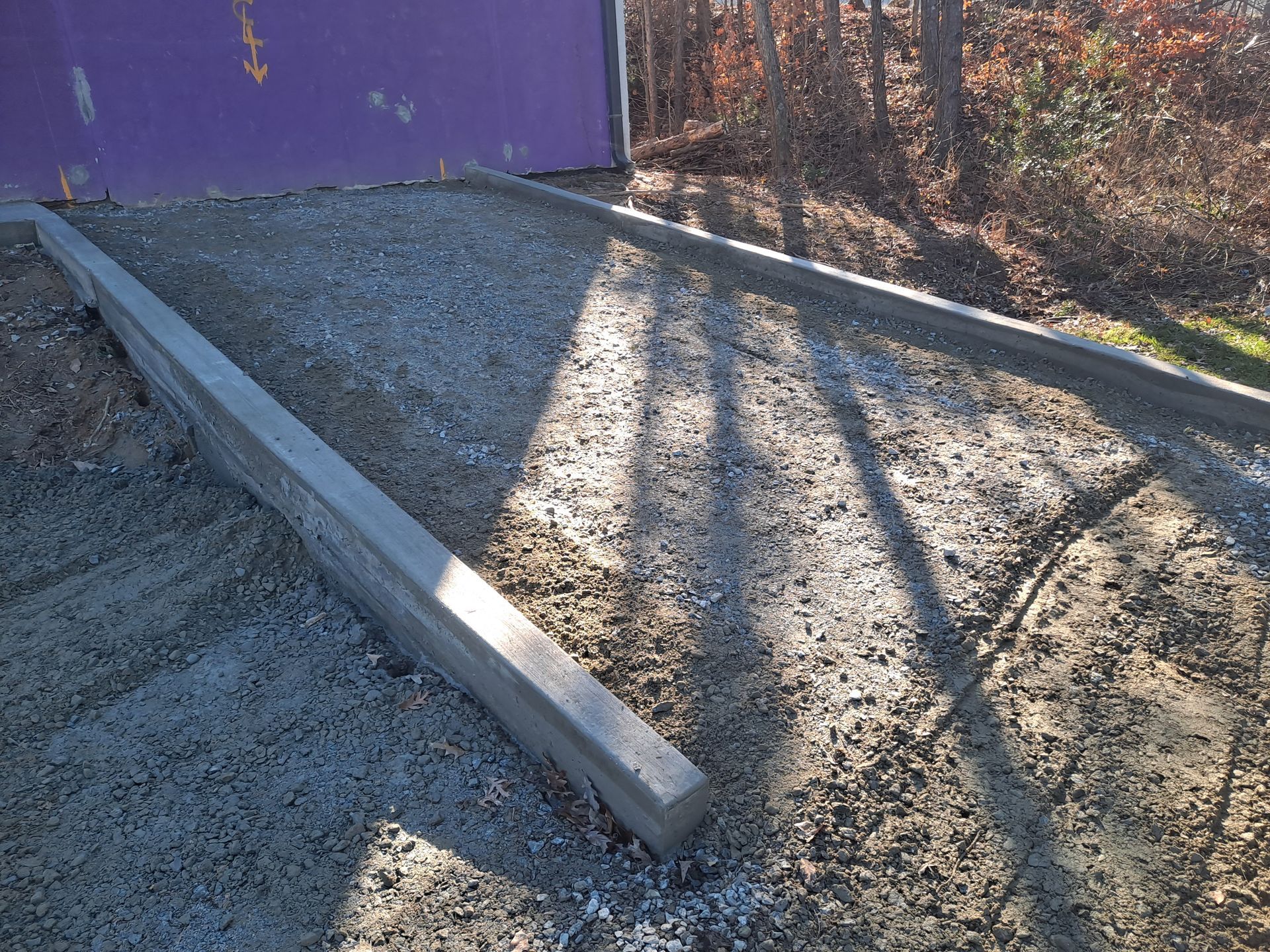 A concrete beam is sitting in the dirt near a purple wall