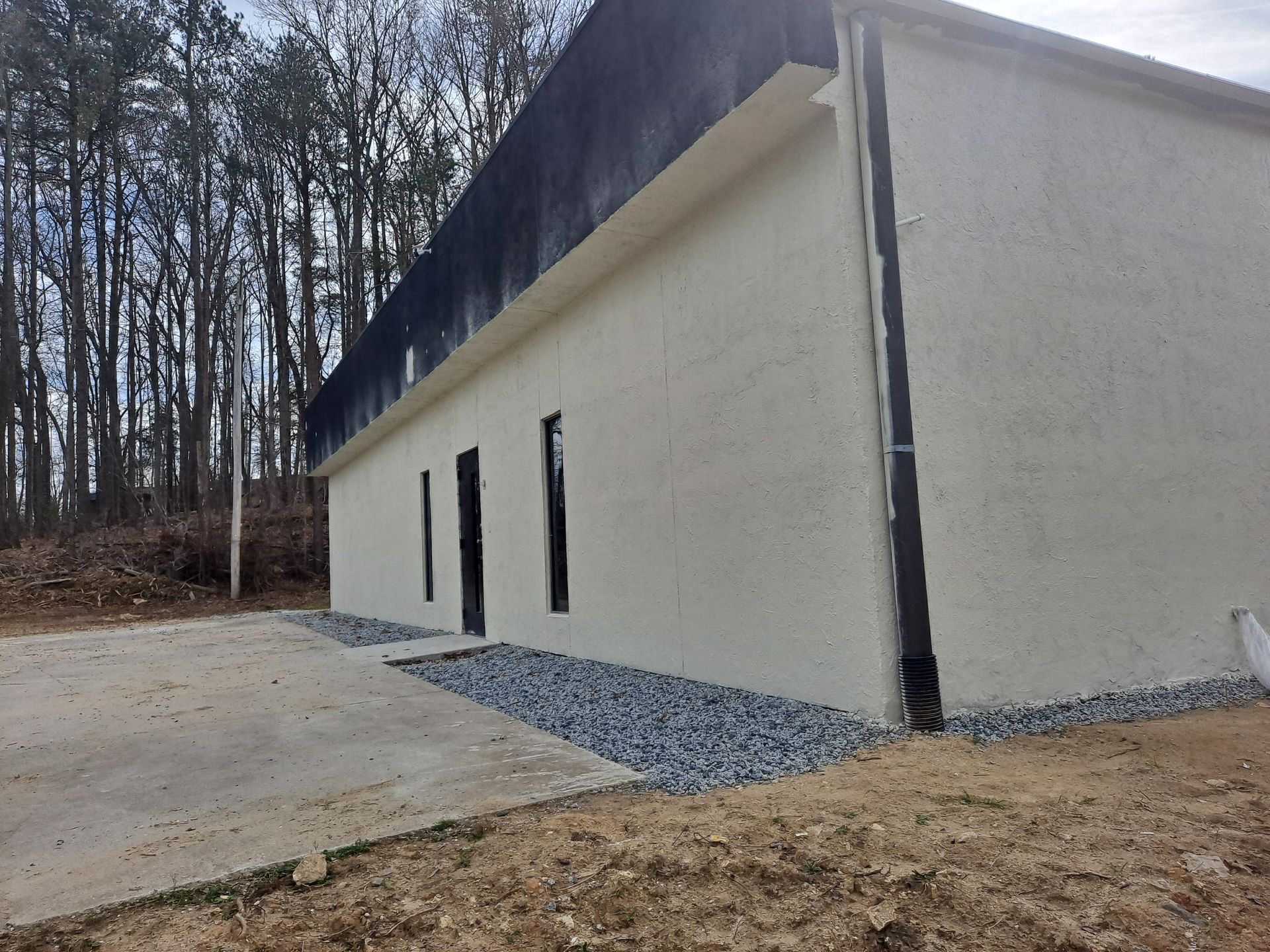 A white building with a black roof is in the middle of a forest.
