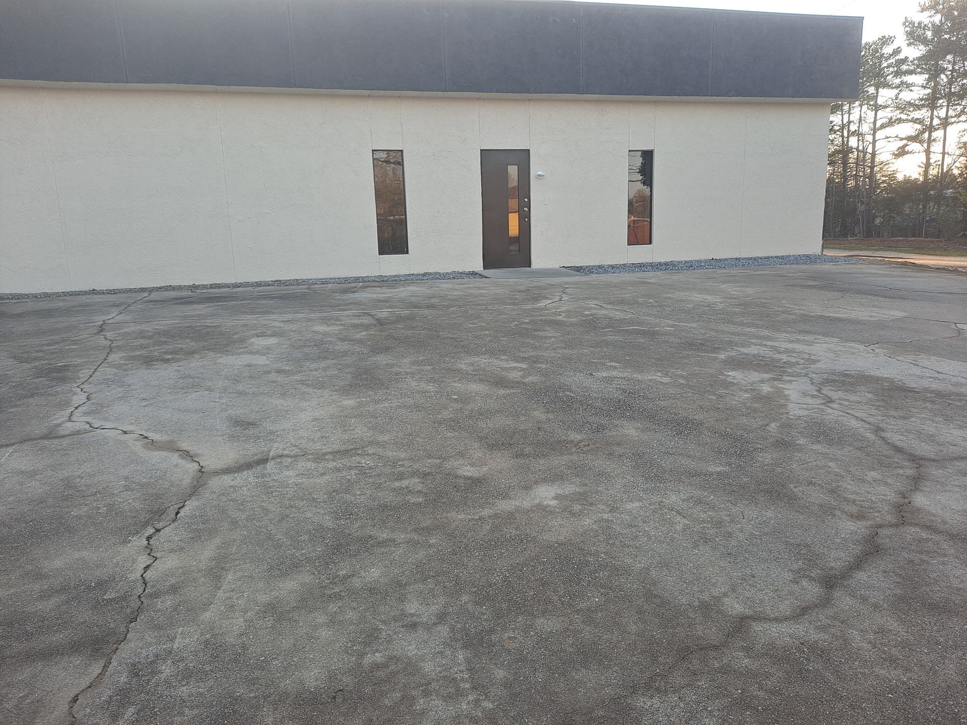 A white building with a black roof and a concrete driveway in front of it.