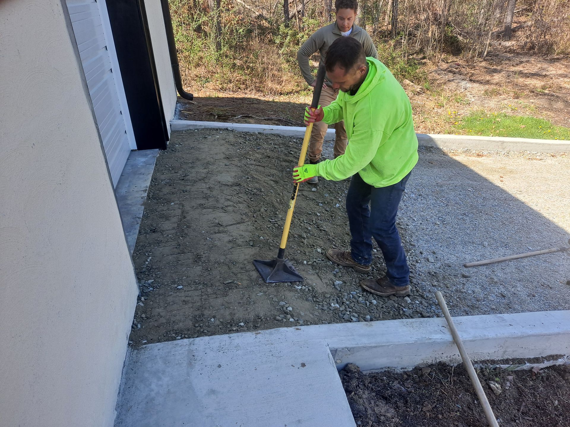 A man in a neon green jacket is digging in the dirt with a shovel.