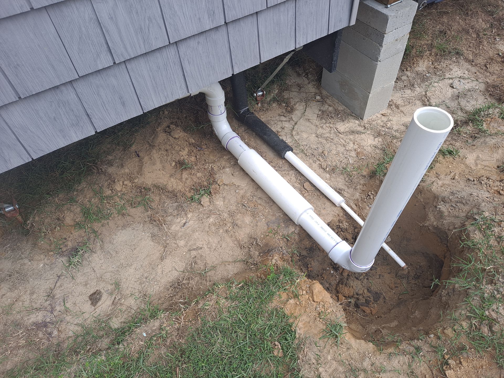A white pipe is sitting in the dirt next to a house.