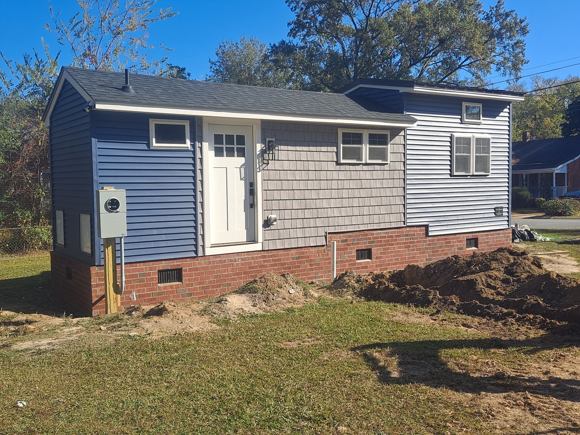 A small house with a blue siding and a white door is sitting on top of a lush green field.