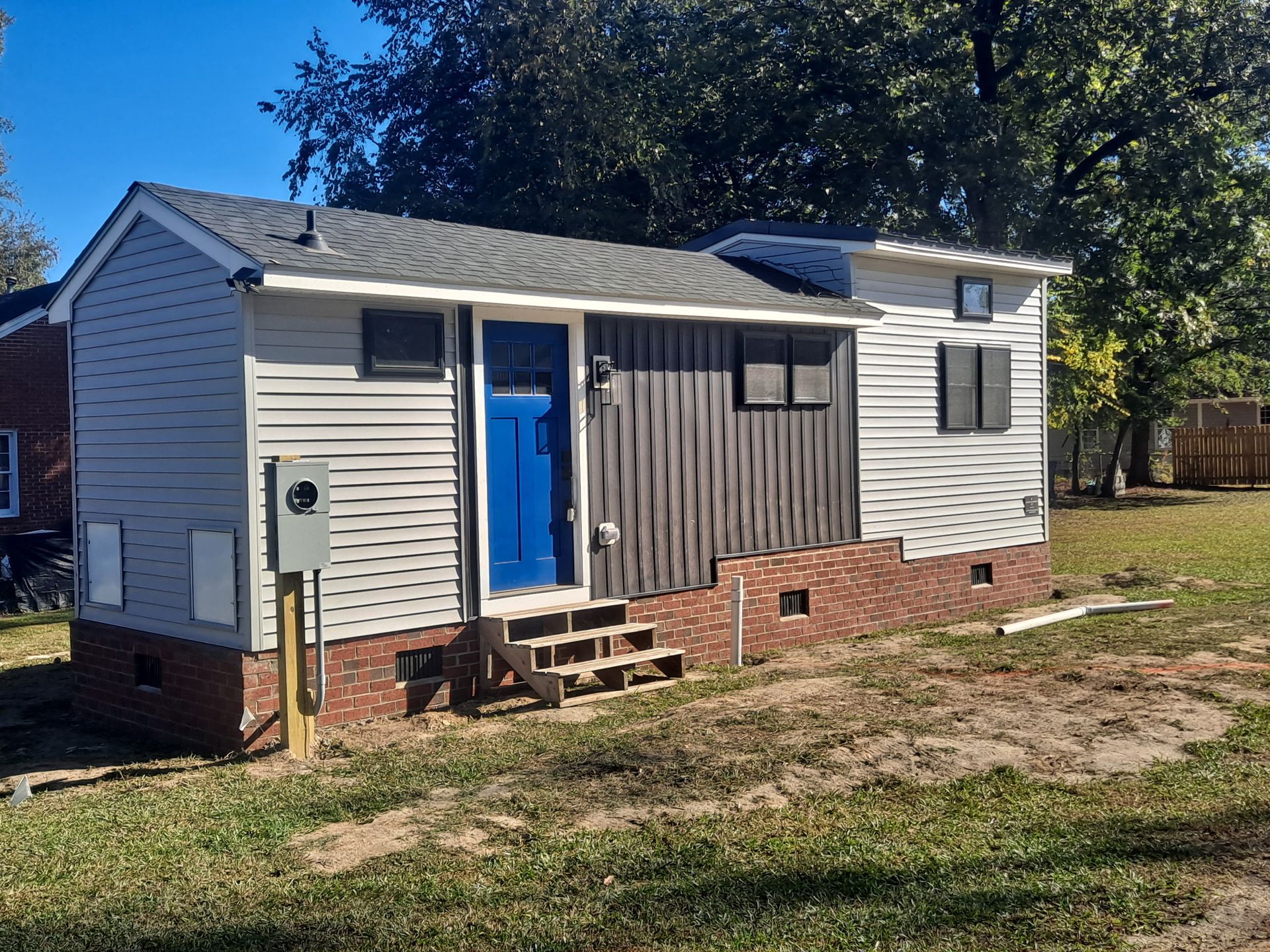 A small white house with a blue door is sitting in the middle of a grassy field.