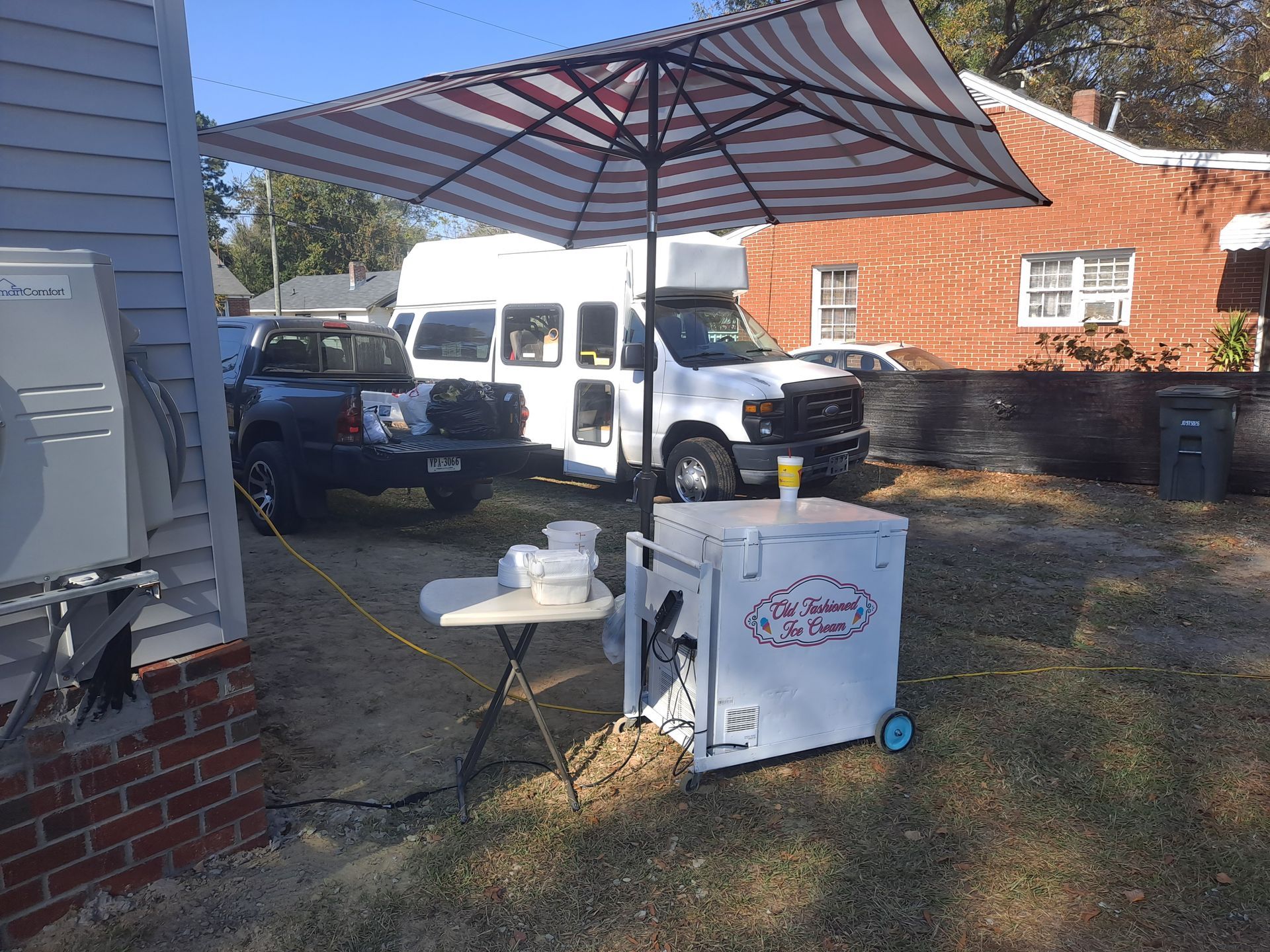 A white truck is parked under an umbrella in front of a brick building.