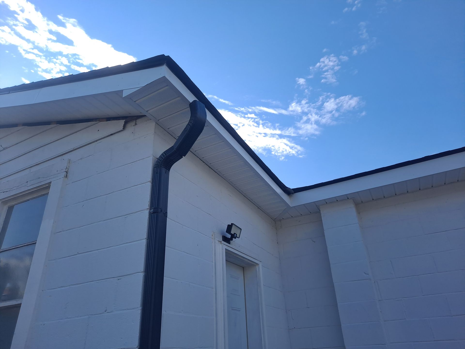 A white house with a black gutter and a blue sky in the background
