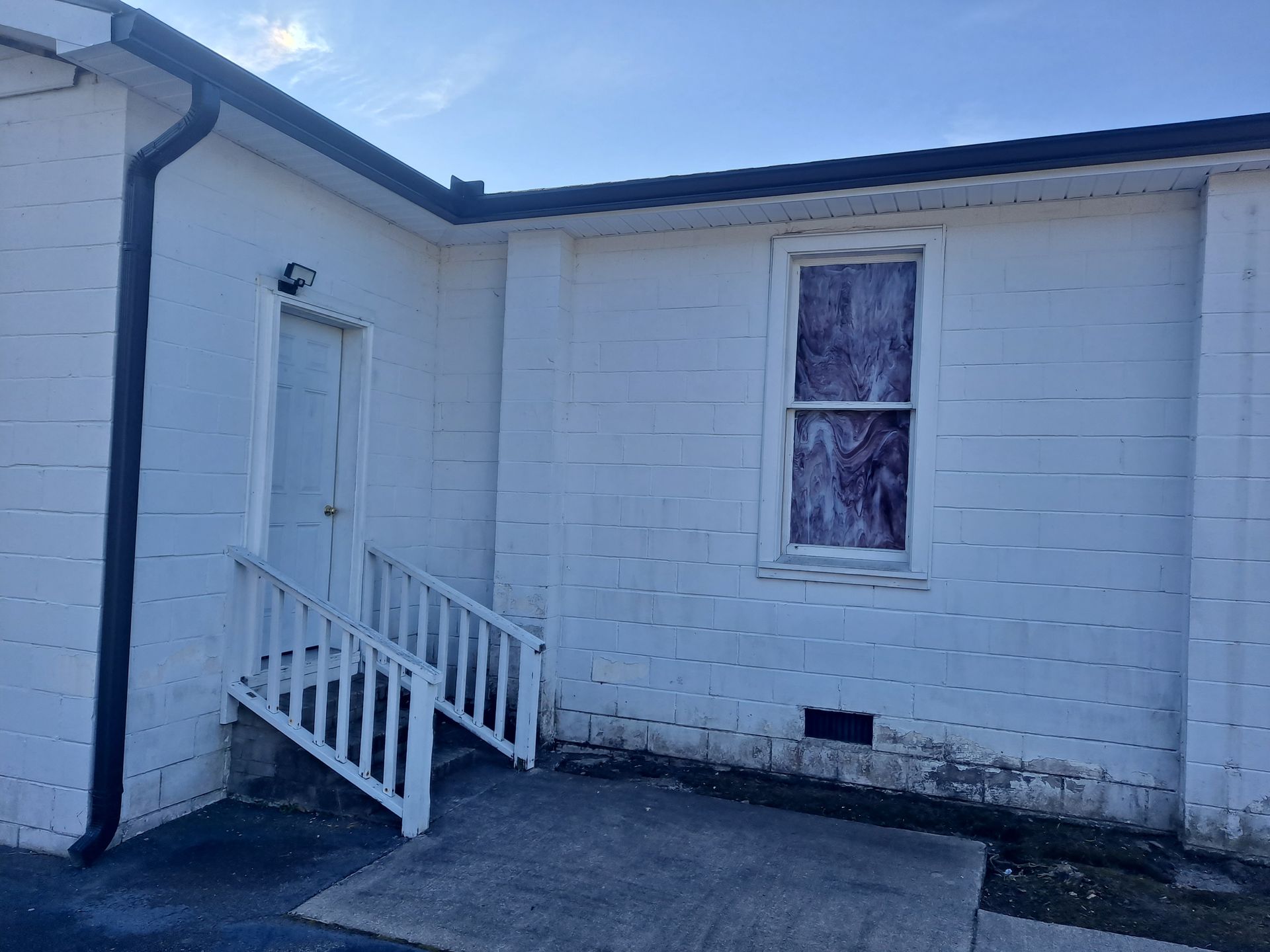 A white brick building with stairs leading up to it and a window.