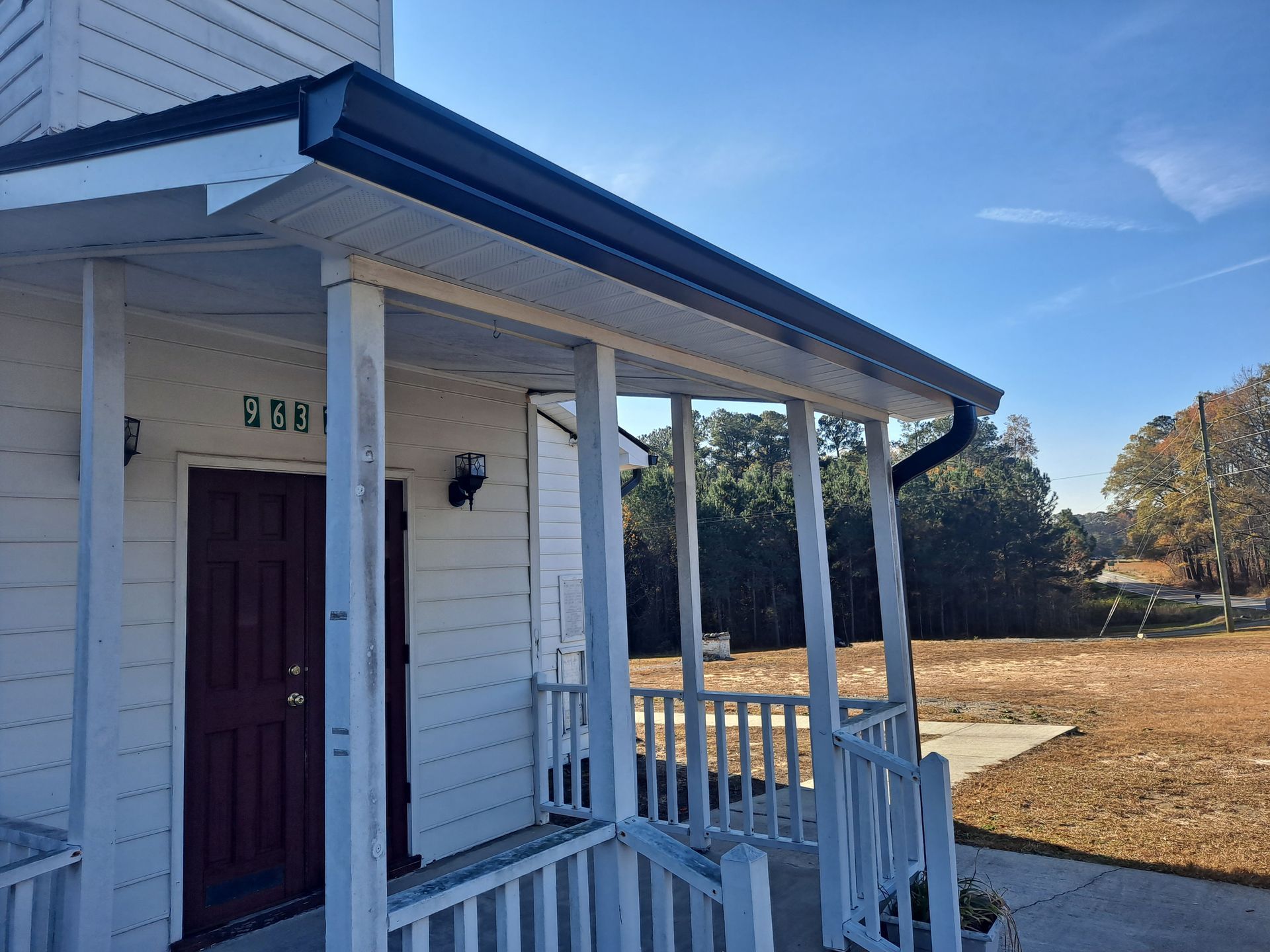 A white house with a porch and a red door on a sunny day.