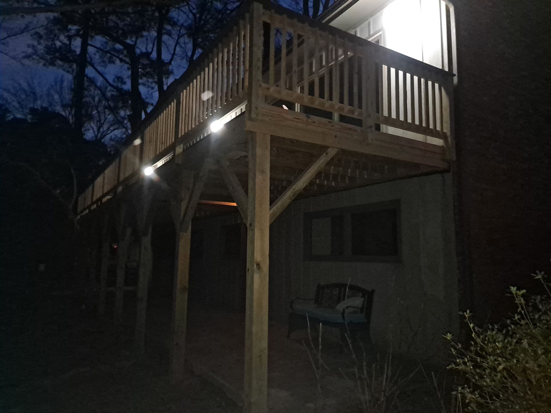 A wooden deck is lit up at night in front of a house.