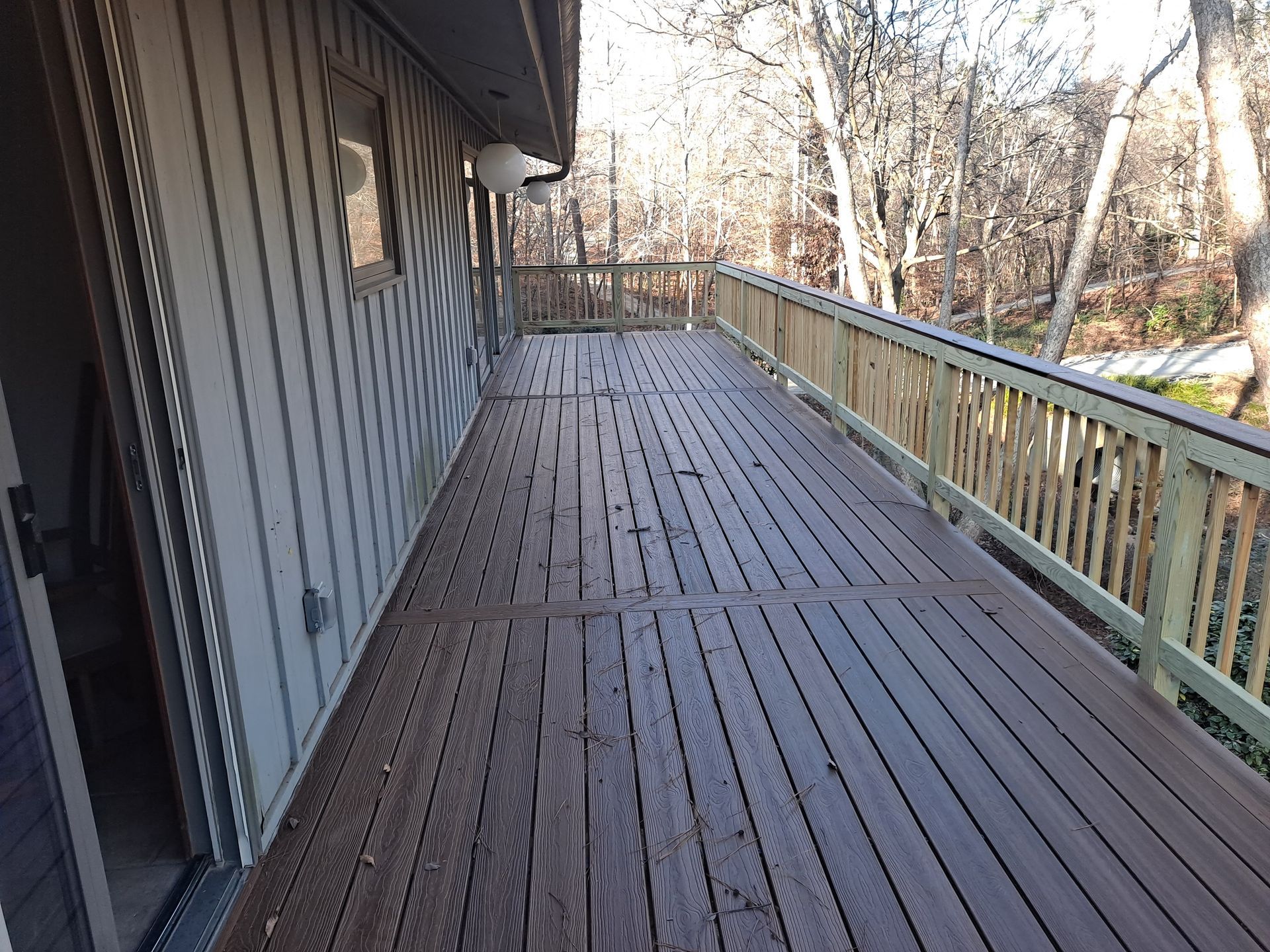 A large wooden deck with a green railing and trees in the background