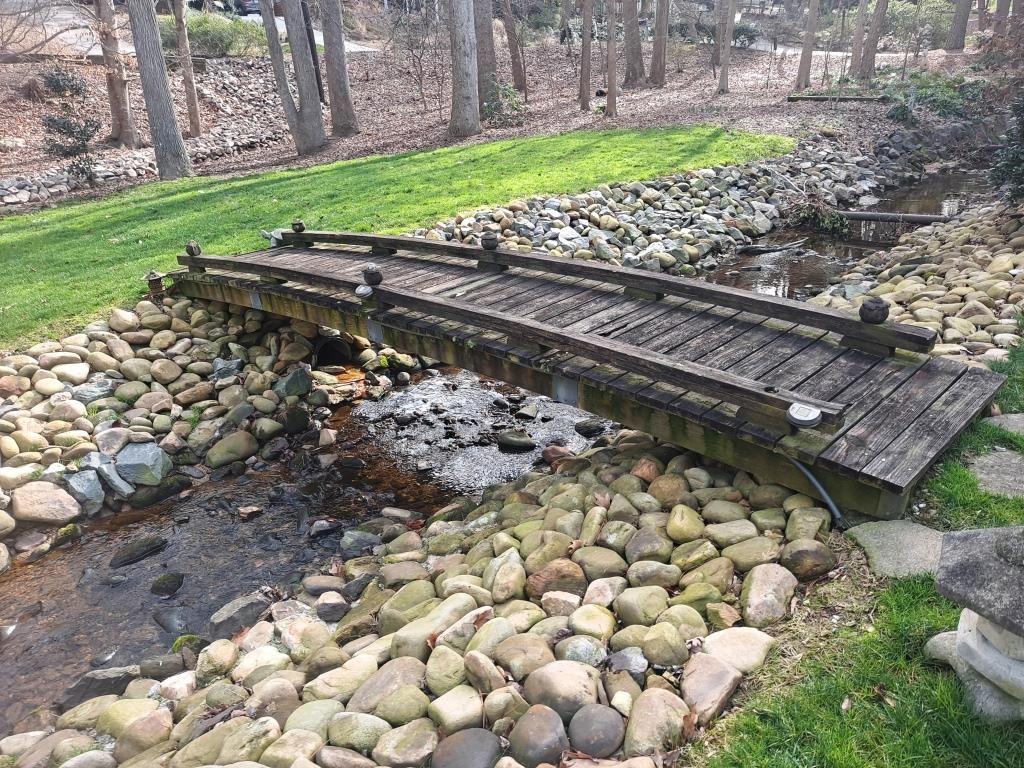 A wooden bridge over a stream in a garden surrounded by rocks.