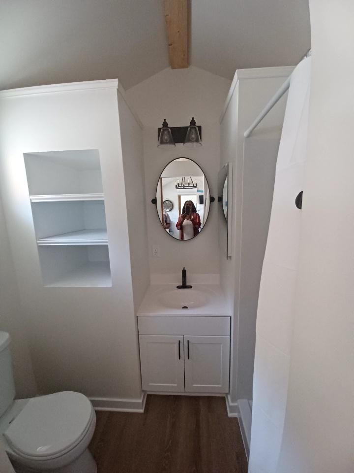 A bathroom with a toilet , sink , mirror and shelves.