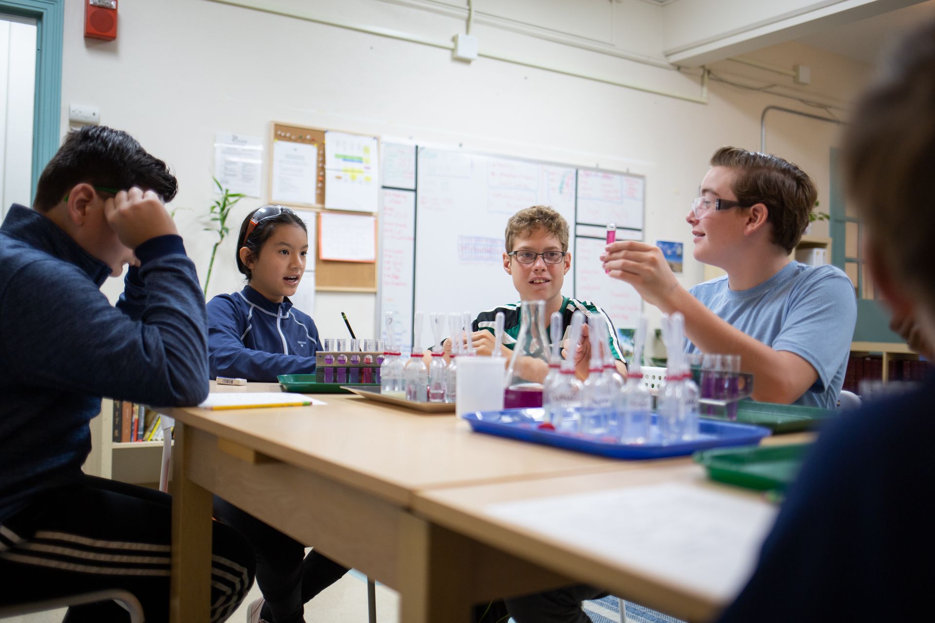 a group of Montessori children are sitting around a table with test tubes on it