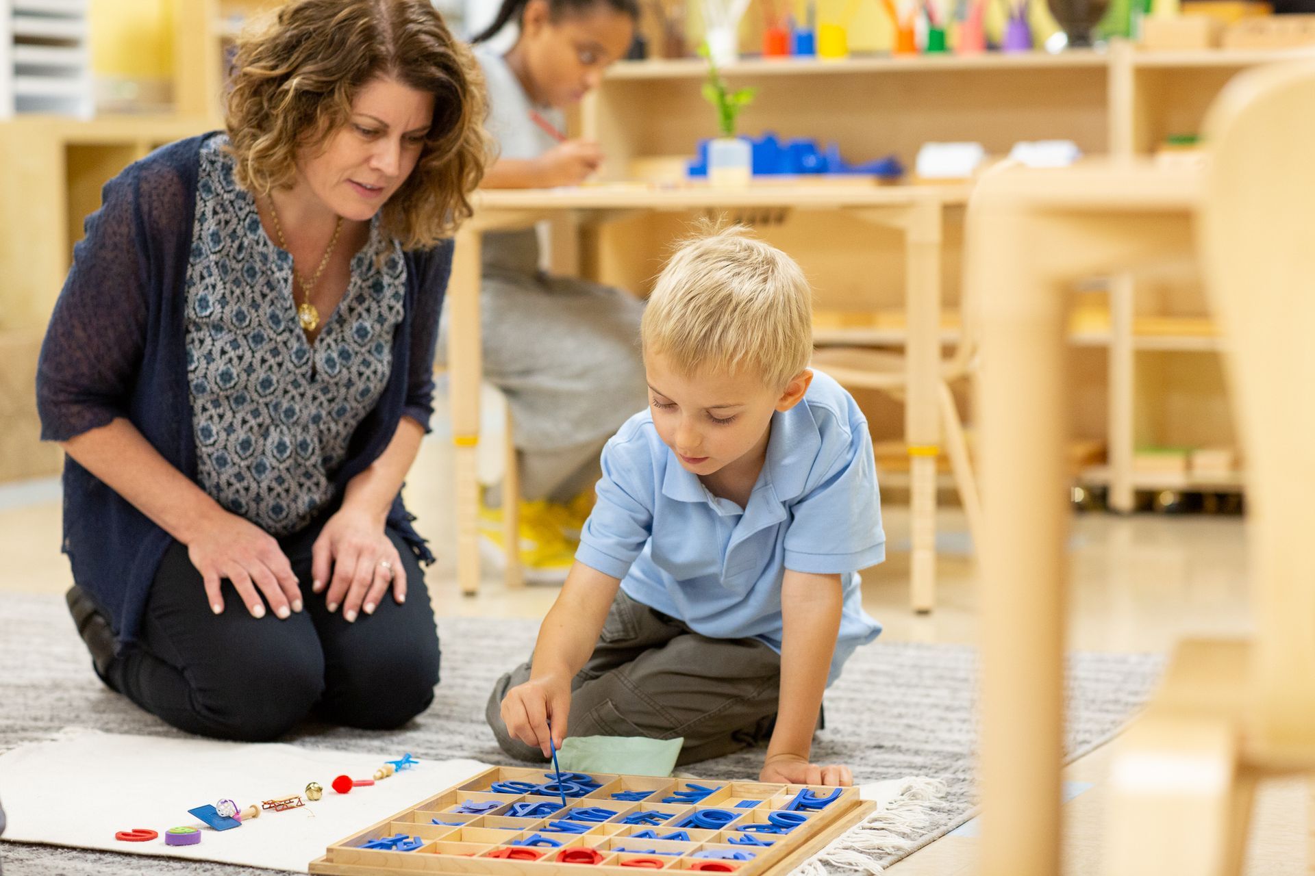 A Montessori guide and a boy are playing with letters on the floor
