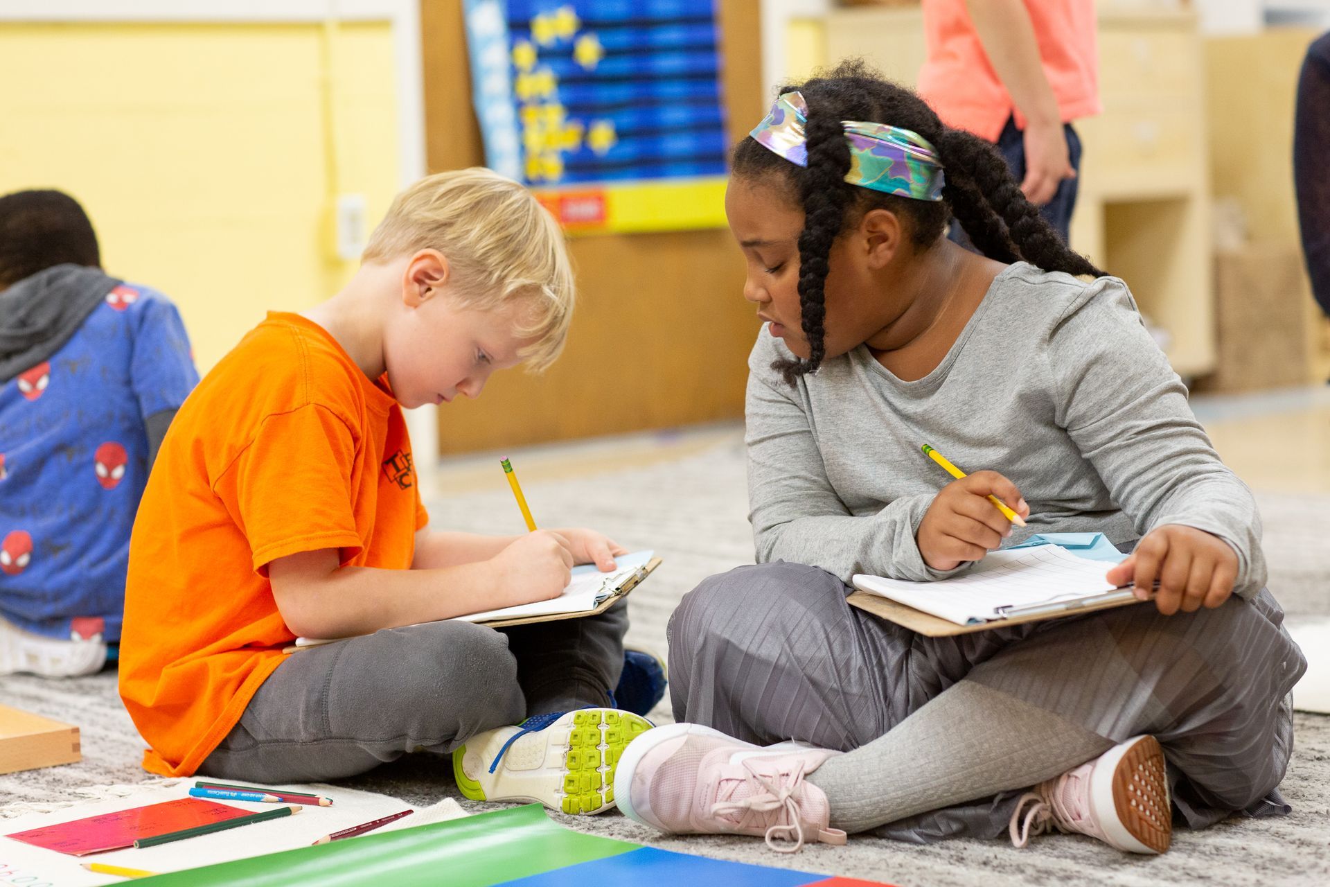 Montessori children are sitting on the floor writing in notebooks