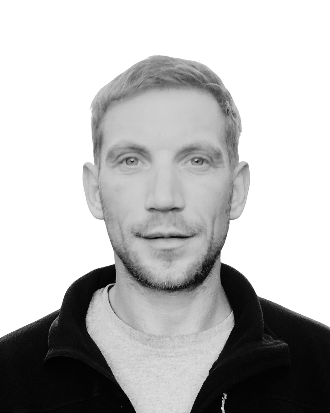 Man with short hair and stubble, wearing a black jacket and gray shirt.