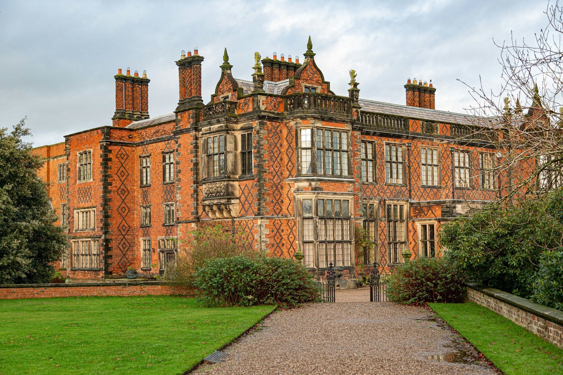 Brick manor house with multiple windows, chimneys, and a gravel path.