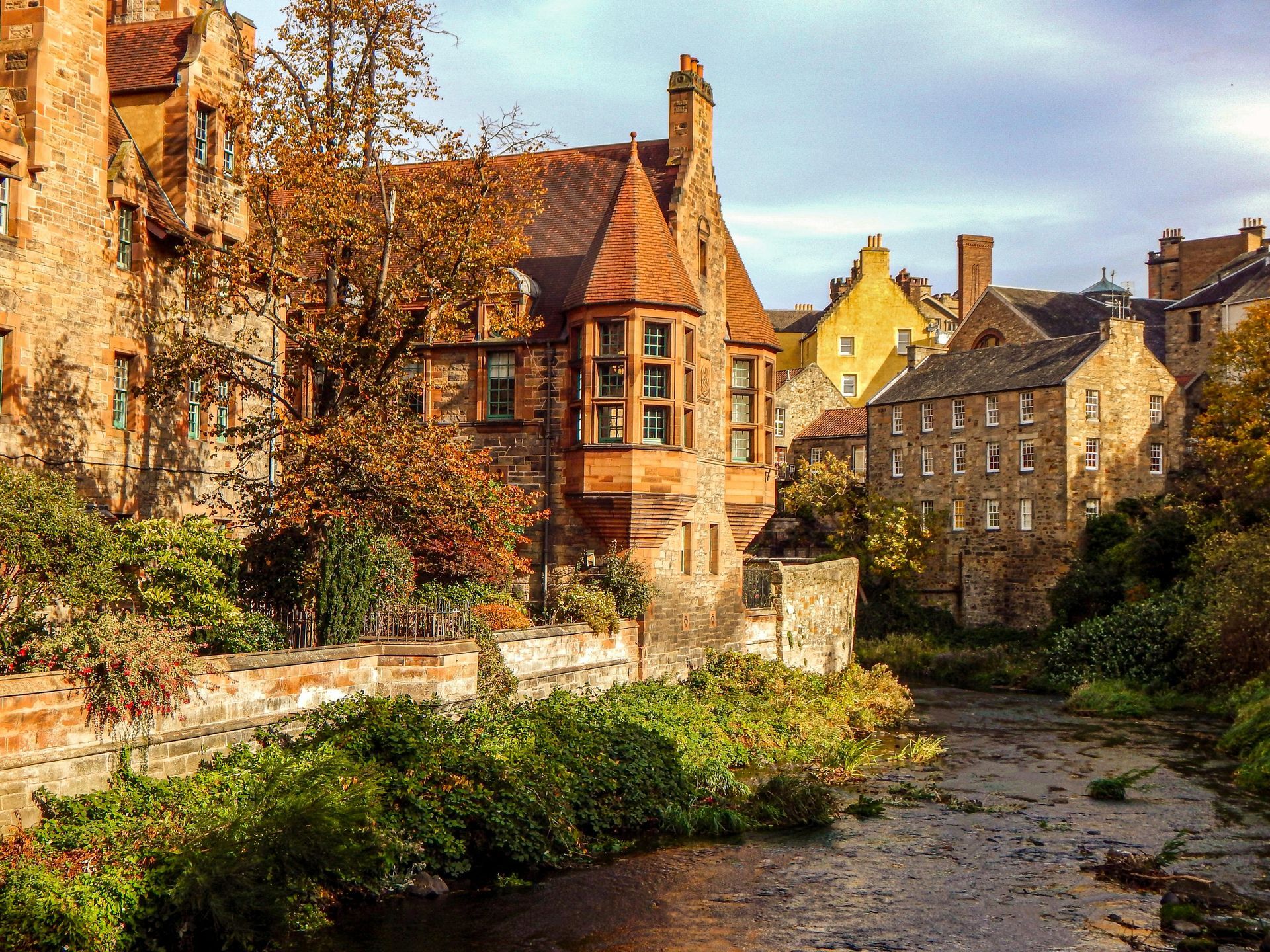 Stone buildings line a river with autumnal trees in Edinburgh, Scotland; overcast sky.