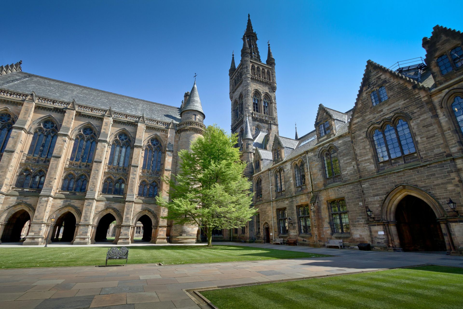 University of Glasgow's historic main building; sandstone architecture, tower, green lawn, blue sky.