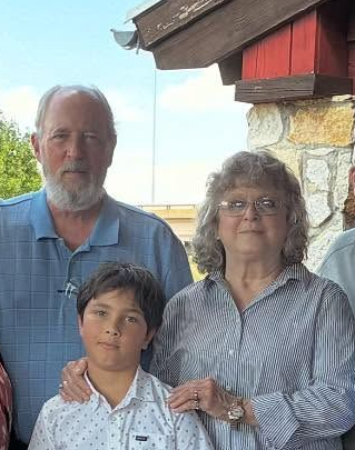 Group of people posing on a porch. Red brick building and a bench are visible.