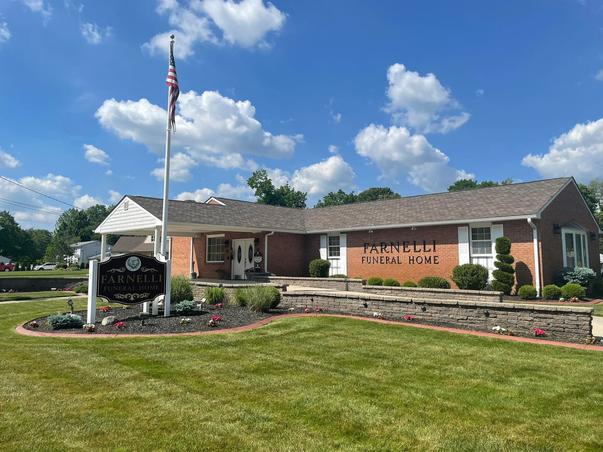 Brick building with white columns, American flag, and landscaped lawn under overcast sky