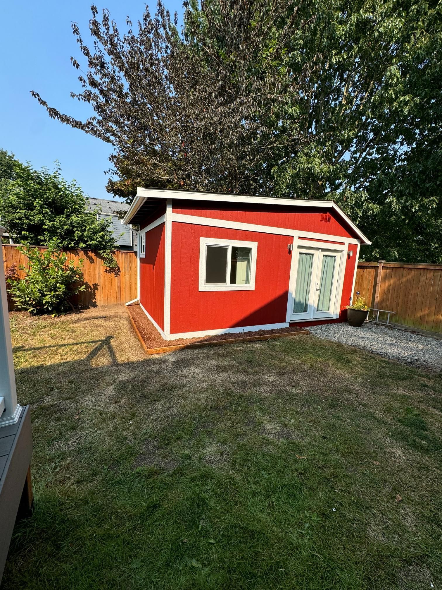 Red shed with white trim, double doors, and a window in a backyard with a grass lawn.
