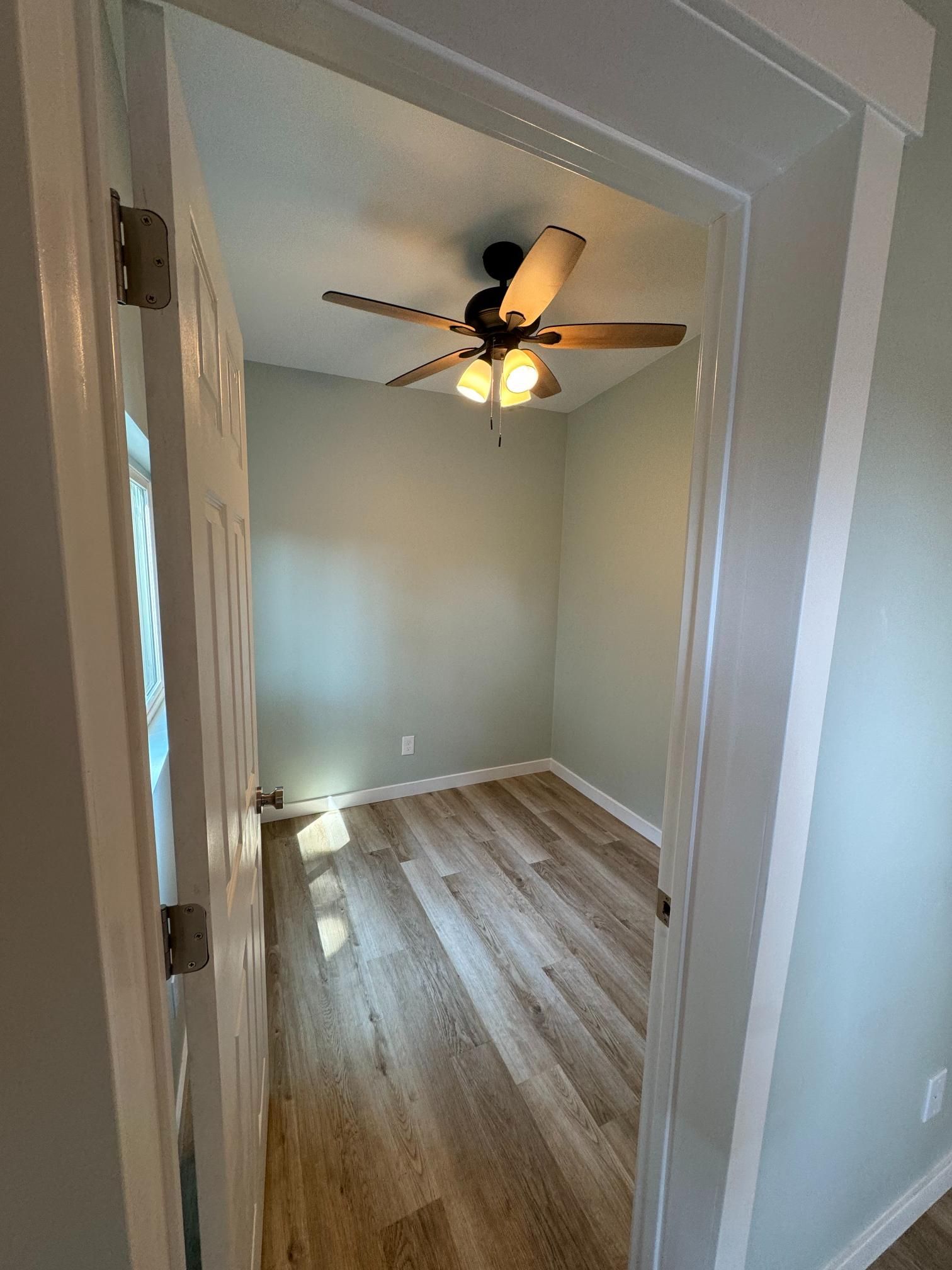 Open doorway into a small room with light wood floors, green walls, and a ceiling fan.