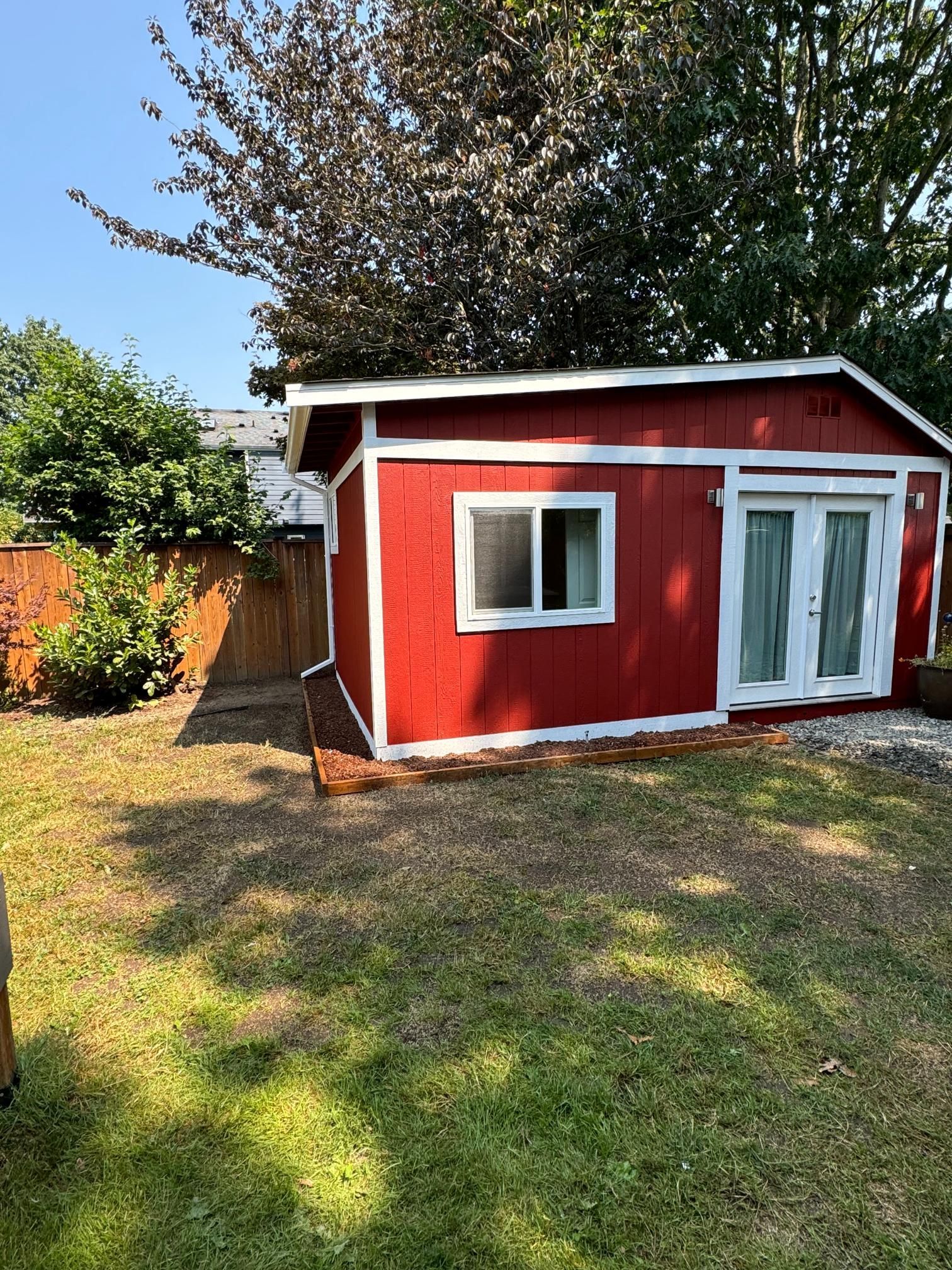 Red shed with white trim, a window, and double doors in a grassy backyard.